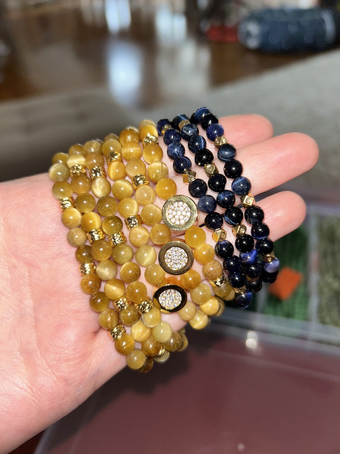 Many Blue, Honey, and Tiger's Eye Bracelets displayed by hand